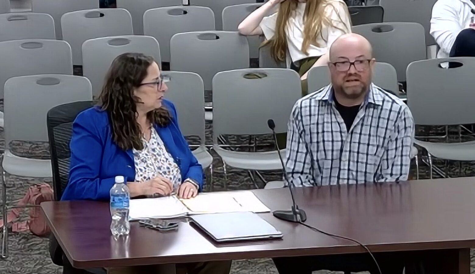 Christopher Knoth and his lawyer sit at a table in front of microphones at a state committee hearing.