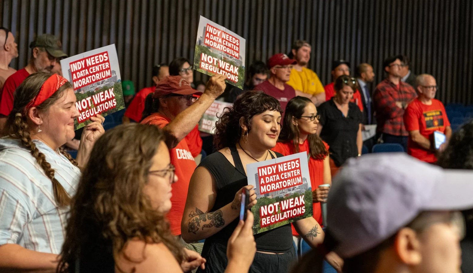 A crowd of people with some of them holding signs protesting data center construction