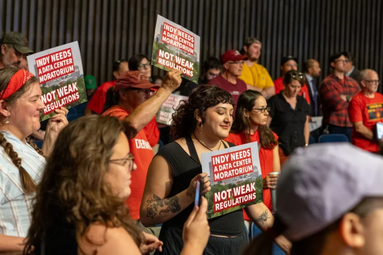A crowd of people with some of them holding signs protesting data center construction