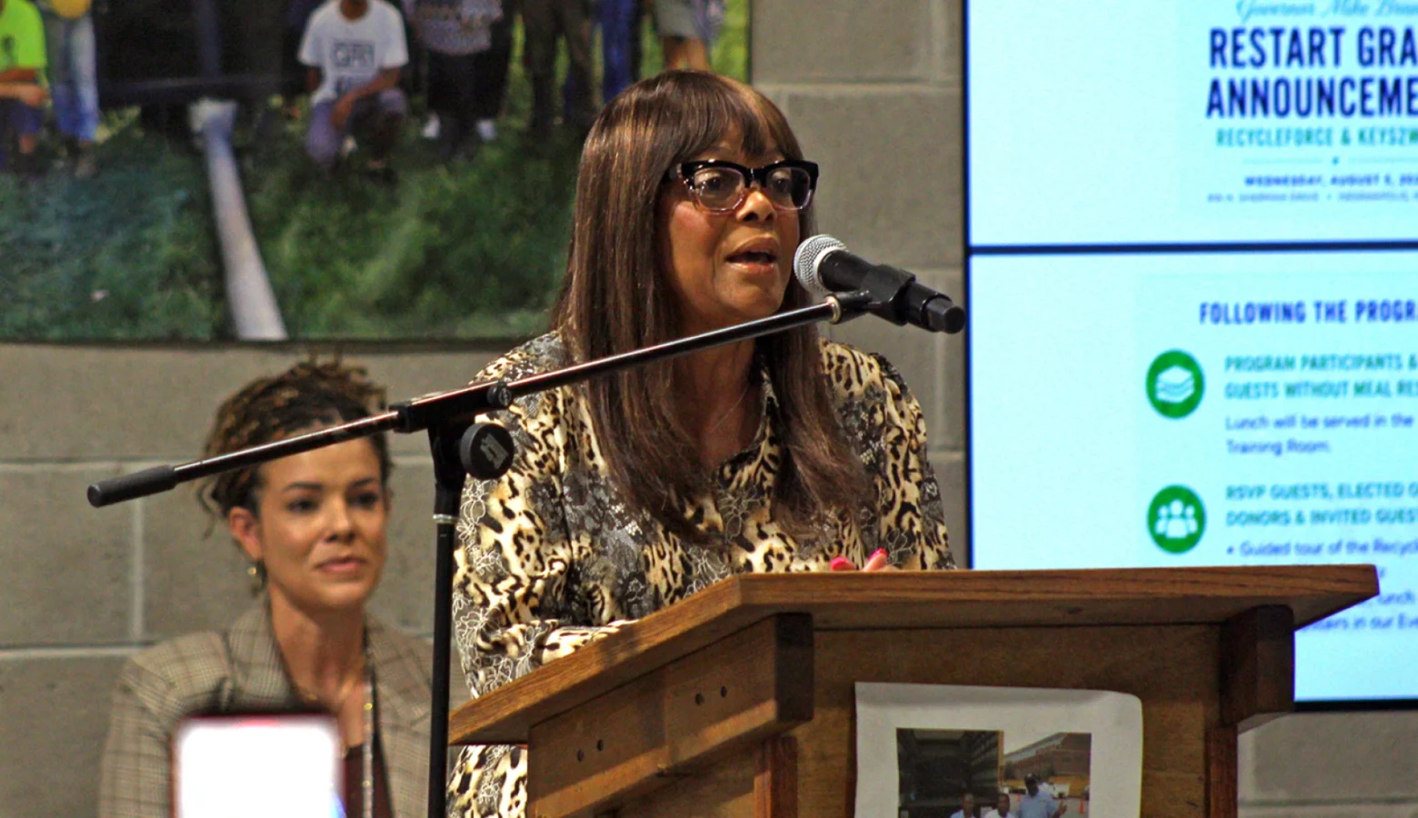 Jannette Keesling at Recycleforce stands at a podium and speaks about a new multi-million dollar grant for the organization.