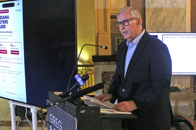 Greg Ballard stands at a podium during a press conference, speaking to the media.