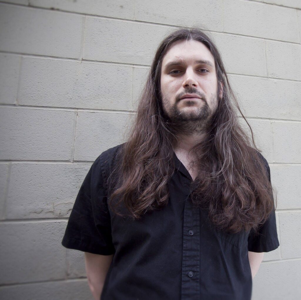 Caleb McCoach standing in front of a cinder block wall