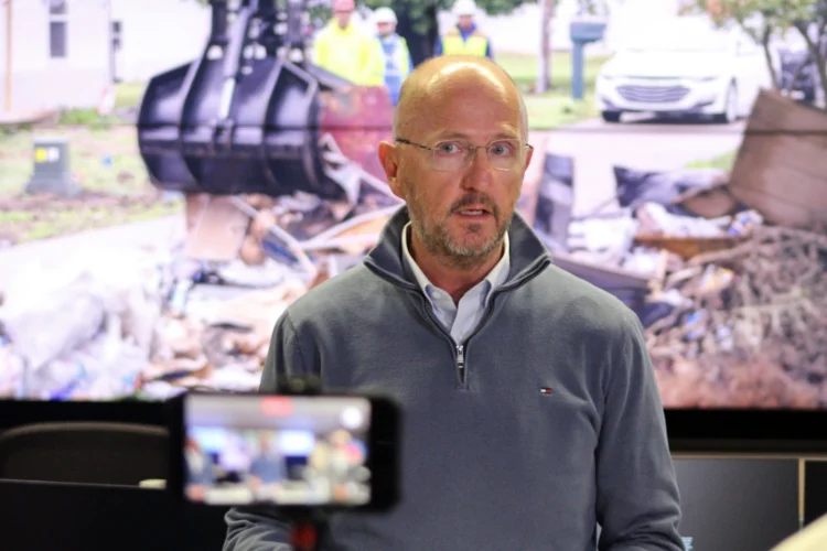 Kevin Guthrie is leading the state’s debris removal task force. He said Indiana’s recovery effort could become the “textbook” for how to manage a natural disaster. Guthrie is dressed in a gray sweatshirt standing in front of a projection screen showing an excavator scooping wreckage.