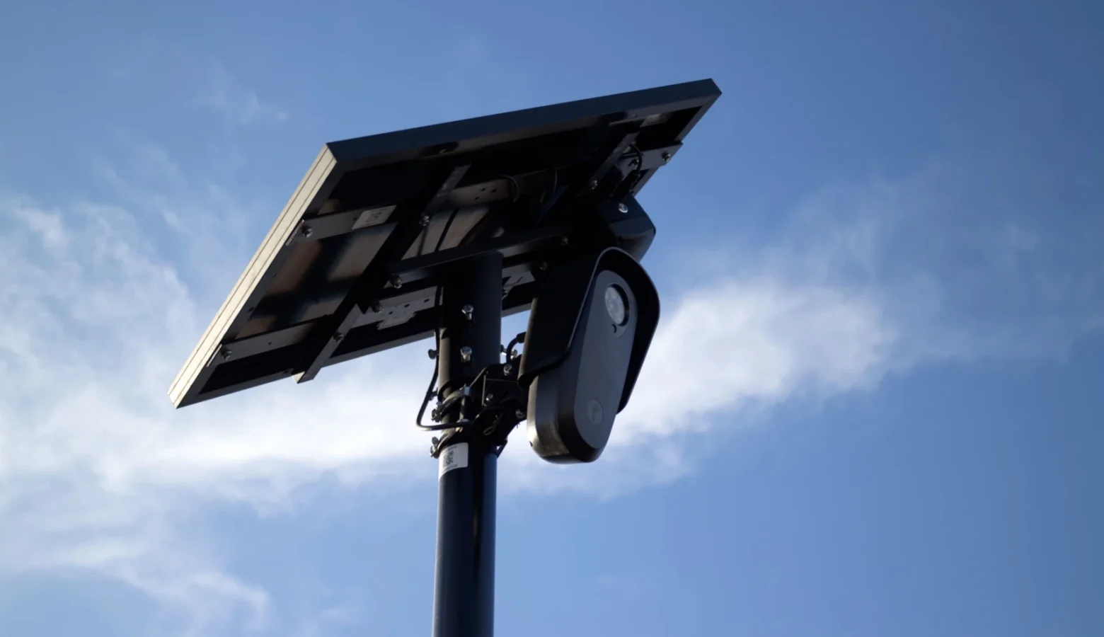 A Flock camera looks forward as its solar panel is aimed toward the sun and a partly sunny sky.