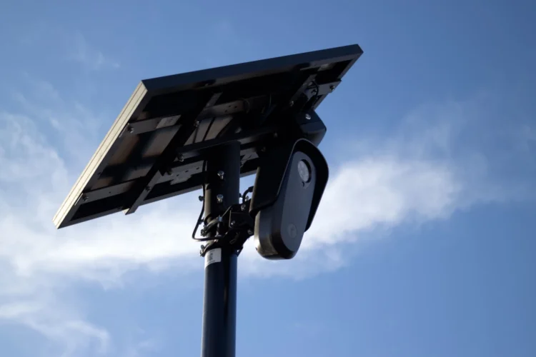 A Flock camera looks forward as its solar panel is aimed toward the sun and a partly sunny sky.