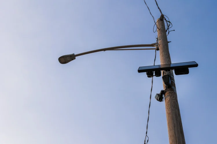 Flock's license plate-reading cameras have spread around the country. This one sits near Promenade Park in downtown Fort Wayne. City council is evaluating whether to continue their contract with the company. The camera is affixed to a utility pole. The photo is looking upward toward a blue sky.