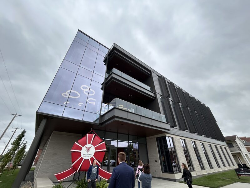 The outside of a large building. In front of it is a massive novelty red ribbon decoration.