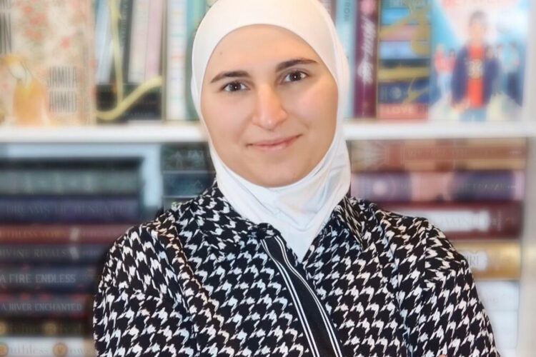 Shifa Saltagi Safadi stands in front of a large display of books with her arms crossed and a slight smile.