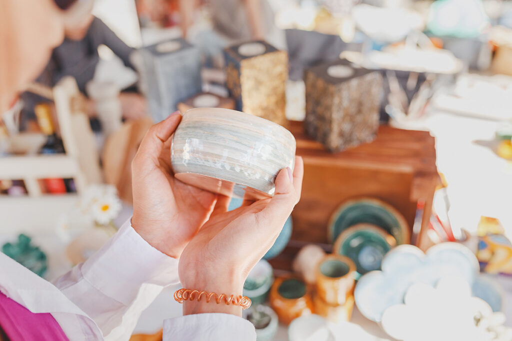 Person holding a ceramic bowl with pottery displayed in the background.