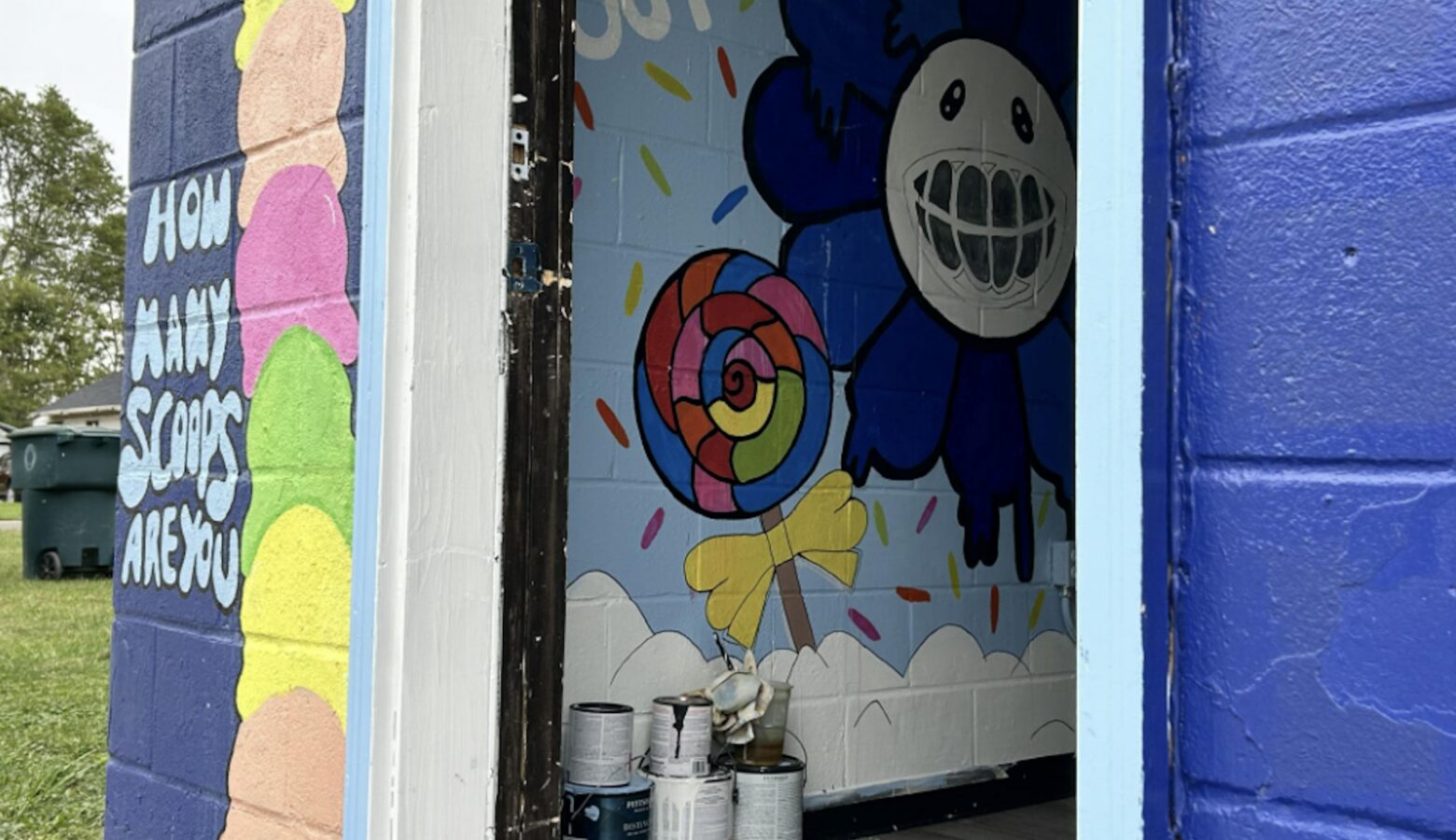 A building with an open door showcases hand-painted murals of ice cream cones and happy flowers and candy.