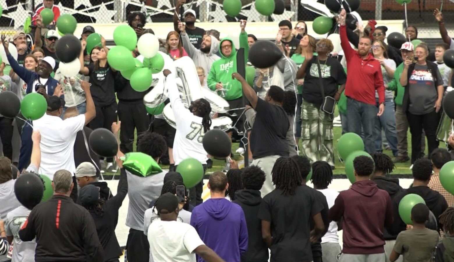 A crowd of people release green balloons at a prayer vigil.