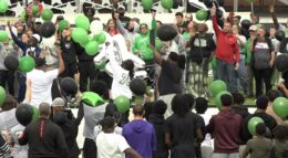 A crowd of people release green balloons at a prayer vigil.