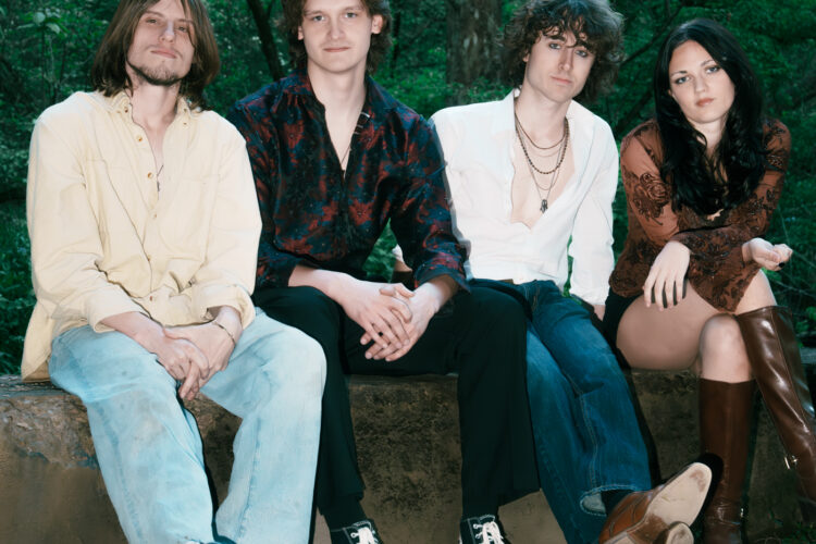 The members of Free Joel; four young people (three men, one woman) sit on a concrete bench with dense greenery behind them. They are wearing casual clothes and neutral expressions.