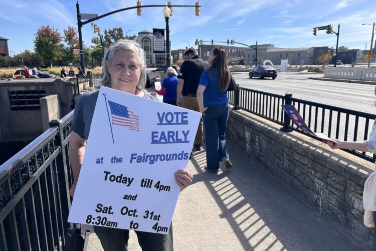A woman holds a sign listing voting information.