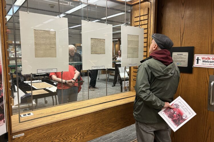 A person stands looking at historic documents hung on a display at Ball State's Bracken Library.