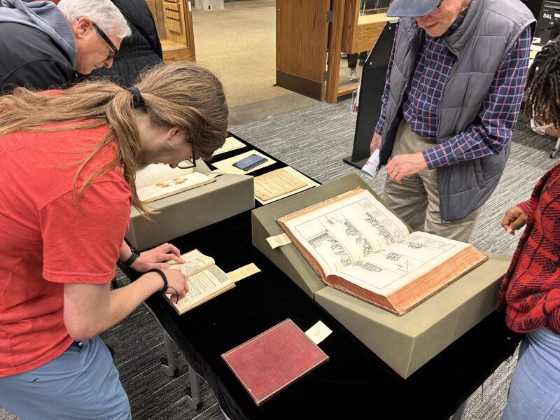 Several people bend over a display to read open pages of historic books.