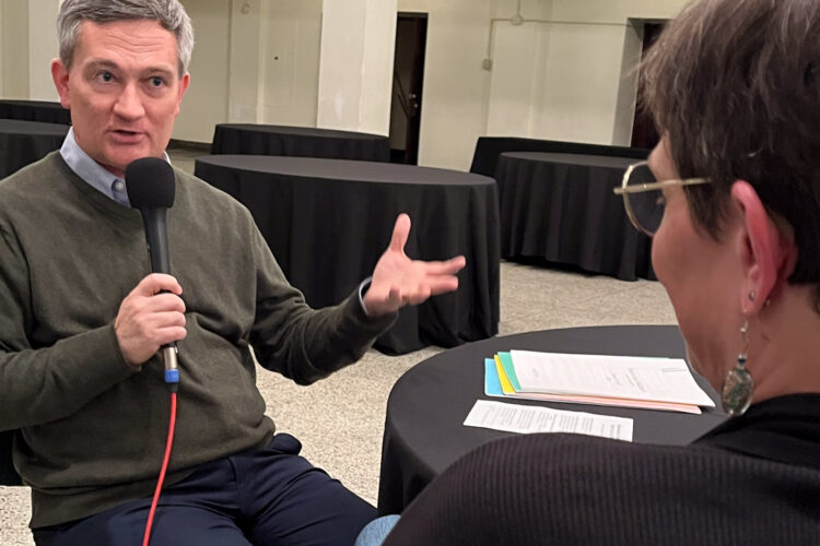 Kerry Glann talks with Jen Blackmer in the middle of an empty banquet hall. He is holding a microphone and gesticulating.