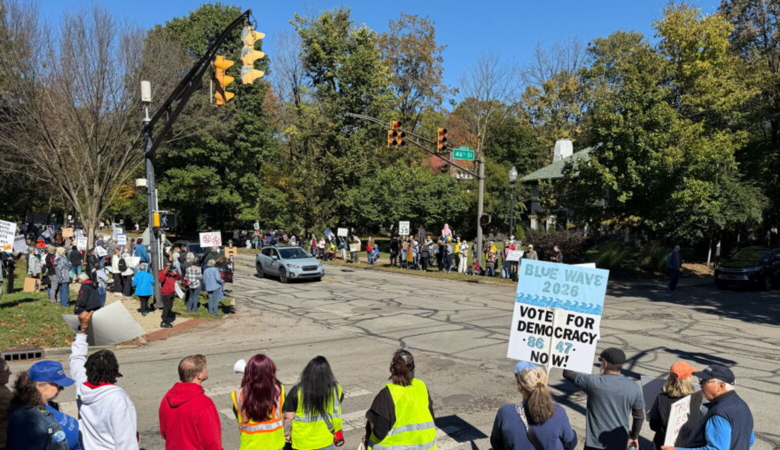 More than 100 people gathered outside the official residence of Gov. Mike Braun in Indianapolis, Sat., Oct. 17 for a "No Kings: Vote Early" rally urgins voters to turn out in the November midterm elections. The intersection of Meridian and 46th streets has protesters holding a variety of signs on sidewalks along the intersection on a sunny day.