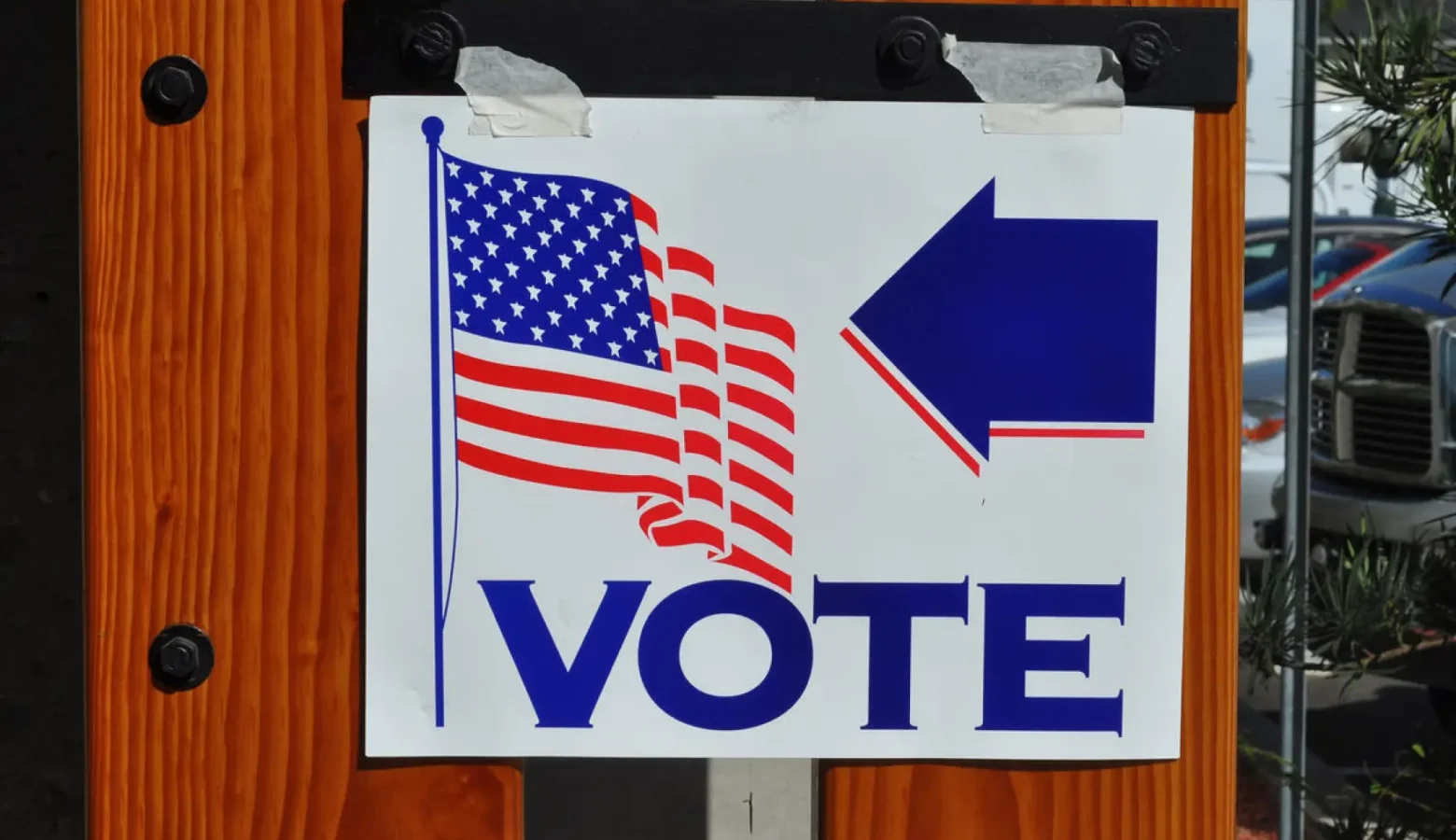 A white sign taped to a door displays the American flag, the work "VOTE," and a blue arrow pointing to the right.
