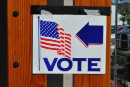 A white sign taped to a door displays the American flag, the work "VOTE," and a blue arrow pointing to the right.