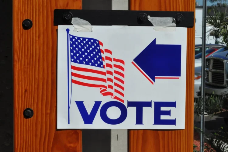 A white sign taped to a door displays the American flag, the work "VOTE," and a blue arrow pointing to the right.