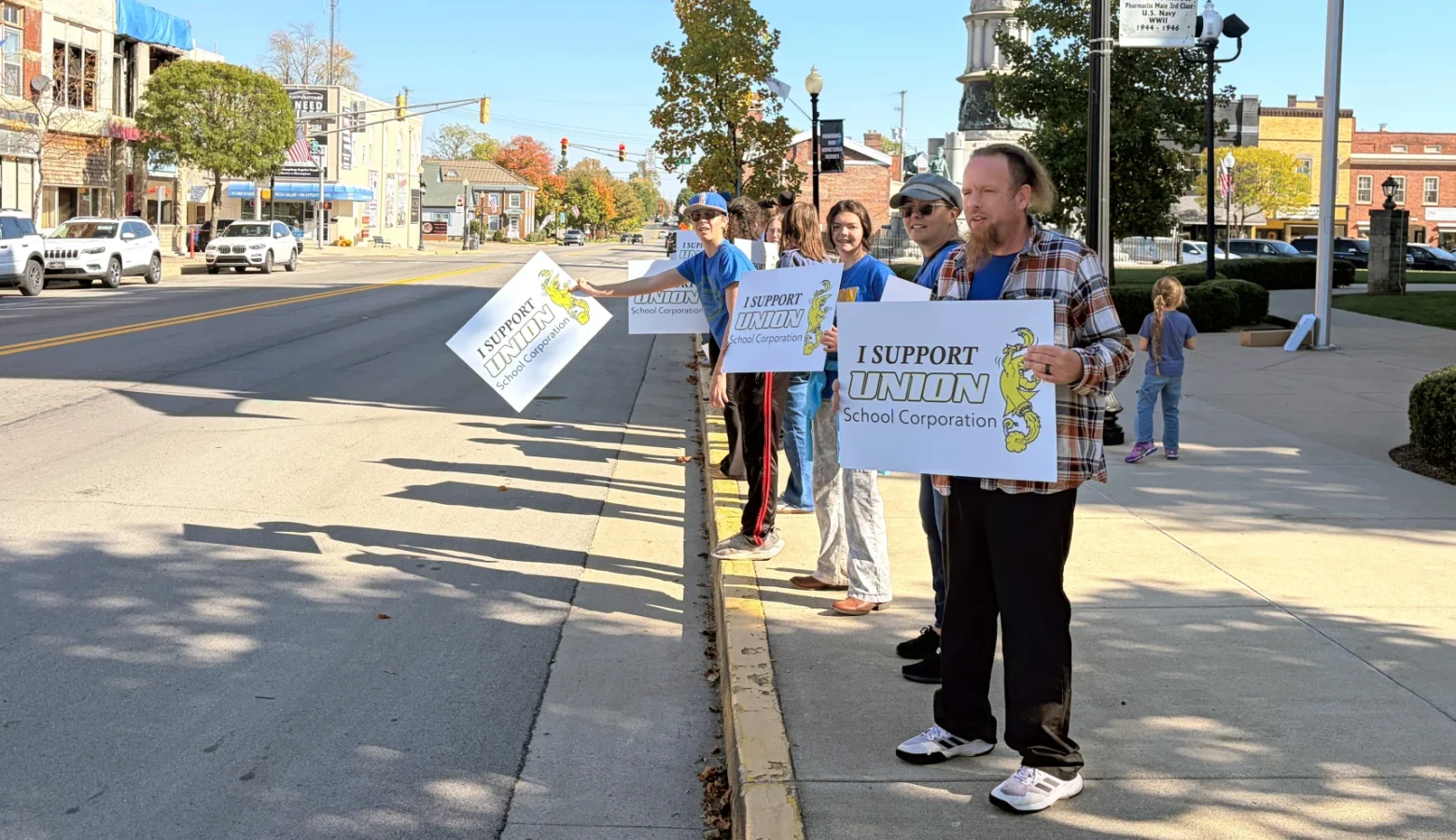 Protesters stand along a road, carrying signs that say I Support Union School Corporation.