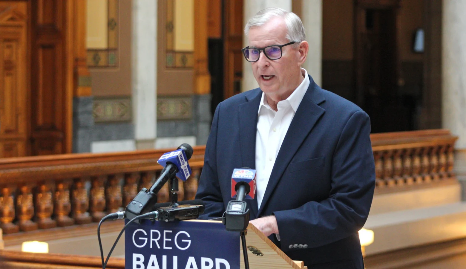 Greg Ballard speaks at a podium in a hallway of the Indiana Statehouse.