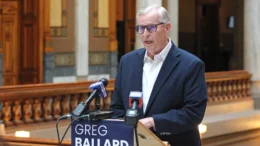 Greg Ballard speaks at a podium in a hallway of the Indiana Statehouse.