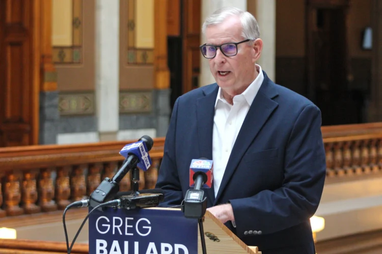 Greg Ballard speaks at a podium in a hallway of the Indiana Statehouse.